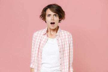 Shocked worried nervous irritated young brunette woman 20s wearing casual basic checkered shirt standing keeping mouth open looking camera isolated on pastel pink colour background, studio portrait.