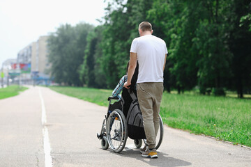 Man rolls wheelchair with girl down street. Relationship with a disabled person and walking together concept