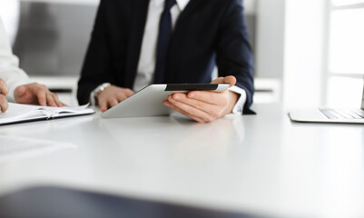 Unknown business people using tablet computer in modern office. Businessman or male entrepreneur is working with his colleague at the desk