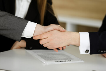 Unknown businessman shaking hands with his colleague or partner above the glass desk in modern office, close-up. Business people group at meeting