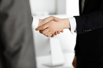 Unknown businessman shaking hands with his colleague or partner while standing straight in modern office, close-up. Business people group at meeting