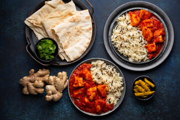 Chicken tikka masala dish with rice, flat Indian bread and spices in rustic metal plates on concrete background top view. Chicken tomato curry, turmeric root, fresh cilantro, traditional Indian meal