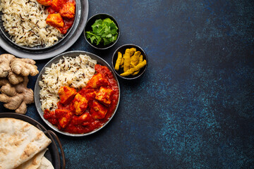 Chicken tikka masala dish with rice, flat Indian bread and spices in rustic metal plates on concrete background top view. Chicken tomato curry, traditional Indian meal, free space for text
