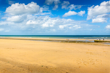 Manche sea, people out digging for razor clams at low tide in afternoon. On long sand beach with cloudy sky