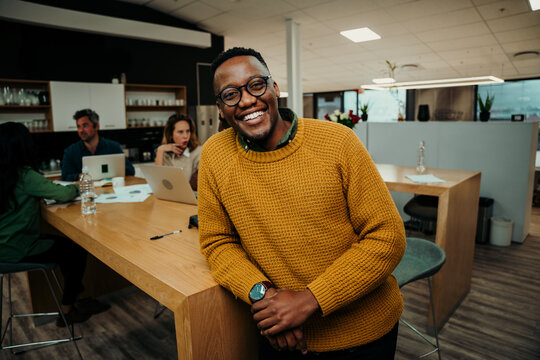 Mixed race business man smiling while enjoying lunch break chatting with colleagues in office lounge