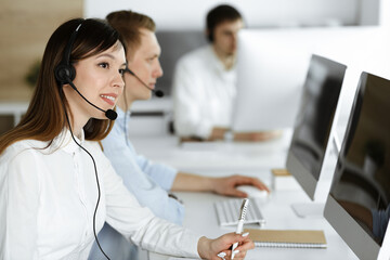 Group of diverse operators at work in call center. Beautiful asian woman sitting in headset at customer service office. Business concept