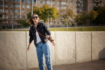 Beautiful young hipster woman in jeans and a jacket in sunglasses walking smiling in the city