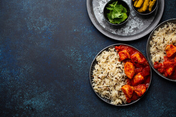 Chicken tikka masala dish with rice, flat Indian bread and spices in rustic metal plates on concrete background top view. Chicken tomato curry, traditional Indian meal, free space for text