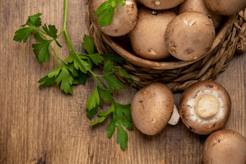 Top view of portobello mushrooms in wooden bowl with parsley on wooden table, horizontal, with copy space