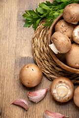 Aerial view of portobello mushrooms in wooden bowl with parsley and garlic on rustic wooden table, vertical, with copy space