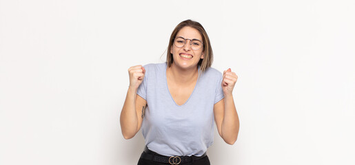 young blonde woman feeling happy, positive and successful, celebrating victory, achievements or...