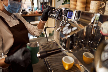 Fototapeta na wymiar Female in medical mask making coffee in coffee shop