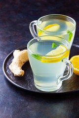 Ginger tea with lemon on a dark background. Two cups of ginger tea on a black plate