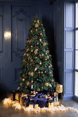 A large tall spruce in the corner of the room with designer decoration and against a dark wall. Luxurious modern decor for Christmas
