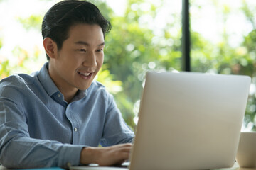 Asian man on blue shirt smiling using a laptop