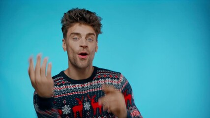Happy young adult man in sweater dancing and pointing with fingers on blue - Powered by Adobe