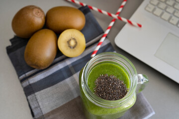 Spinach and kiwi smoothie with laptop and two strip straws on gray background with kiwis.Healthy...