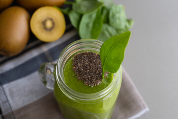 Green smoothie with chia in mason jar on gray background with kiwis and spinach.Detox cocktail, healthy diet concept with spinach, pineapple, kiwi and grapes .
