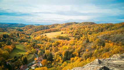 European autumn rural landscape,valley with fields,winding road at bottom,surrounded by hills covered with colorful fall forest,sky with clouds above.Scenic background.Selective focus,blur foreground