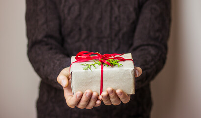 A man in a dark gray sweater is holding a gift box with a red ribbon