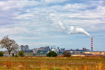 Fototapeta na wymiar The production complex of a cement plant on the horizon behind an agricultural field.