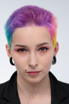 A young beautiful girl with short colored hair. Spread bright coloring and creative make-up. Piercing on the face. A black jacket.