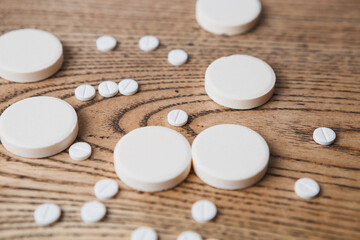 white small and large round pills on a wooden background close-up. Pharmaceutical drugs for the treatment of diseases on a wooden table