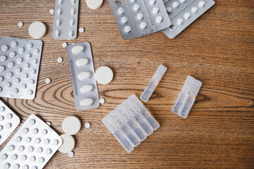 plastic transparent ampoules with liquid medicine and tablets of different sizes, oval and round in blisters and scattered on the table on a wooden background