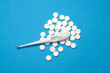 Fototapeta na wymiar group of white pills or tablets and electronic digital thermometer on blue background