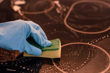 
Hand in a blue rubber glove holds a cleaning sponge and wipes off soap suds on a black background