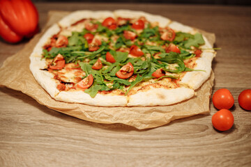 vegan pizza with vegetables on a wooden table in a cafe. Pizza with cherry tomatoes and rucola on food paper on a wooden table with small tomatoes in the foreground and bell pepper in the background