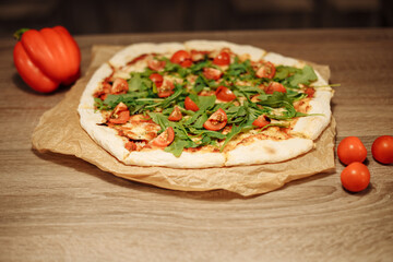 vegan pizza with vegetables on a wooden table in a cafe. Pizza with cherry tomatoes and rucola on food paper on a wooden table with small tomatoes in the foreground and bell pepper in the background