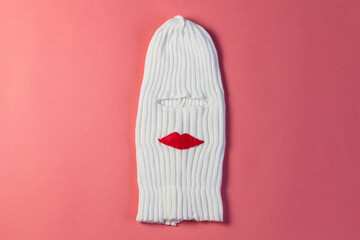 White knitted woolen hat balaclava with hole for eyes, red lips on pink background