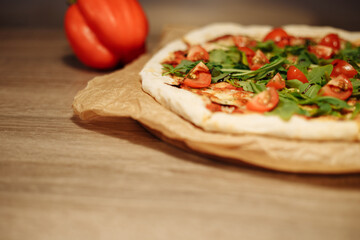 vegan pizza with vegetables on a wooden table in a cafe. Pizza with cherry tomatoes and rucola on food paper on a wooden table with bell pepper in the background