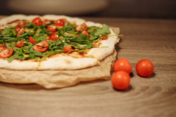 vegan pizza with vegetables on a wooden table in a cafe. Pizza with cherry tomatoes and rucola on food paper on a wooden table with small tomatoes in the foreground and bell pepper in the background