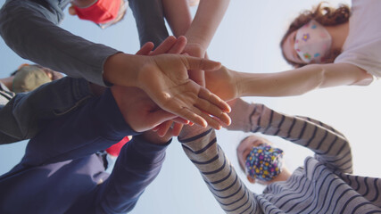 Bottom view of diverse schoolchildren in mask putting hands together outdoors