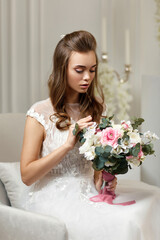 Gorgeous tender young bride with flower bouquet sitting on armchair in white studio interior