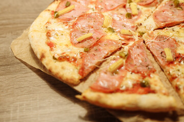 pizza with sausage, mini corn, jalapeno pepper on food paper on a wooden table in warm light
