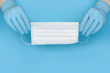 Disposable medical mask in hands in blue rubber medical gloves on a blue background. Healthcare and protection concept.