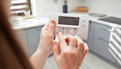 The woman adjusts the thermostat in the house © SkyLine
