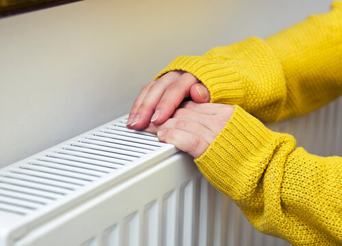 The woman warms her hands on the radiator