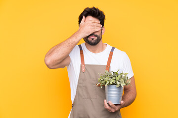 Gardener man with beard over isolated yellow background covering eyes by hands