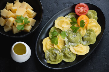 Italian ravioli served with grated parmesan cheese over black stone background, elevated view, horizontal shot