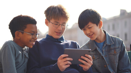 Diverse schoolboys using digital tablet on bench at school outdoors