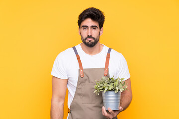 Gardener man with beard over isolated yellow background sad