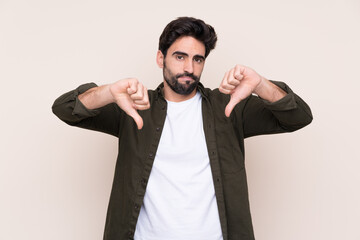 Young handsome man with beard over isolated background showing thumb down