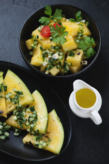 Salad with yellow watermelon, herbed cucumber and fresh parsley, vertical shot on a black stone background, selective focus