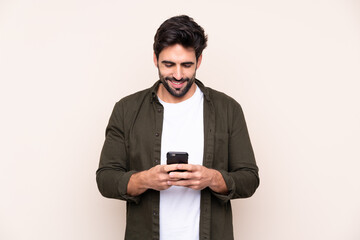 Young handsome man with beard over isolated background sending a message with the mobile