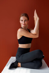 Obraz premium young fitness woman do yoga exercises while sitting on box, she sits with crossed legs and hands, concentrated, smiles at camera