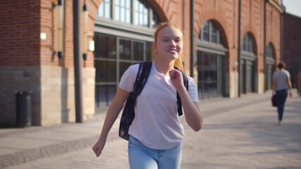 Happy redhead schoolgirl running with backpack after school.